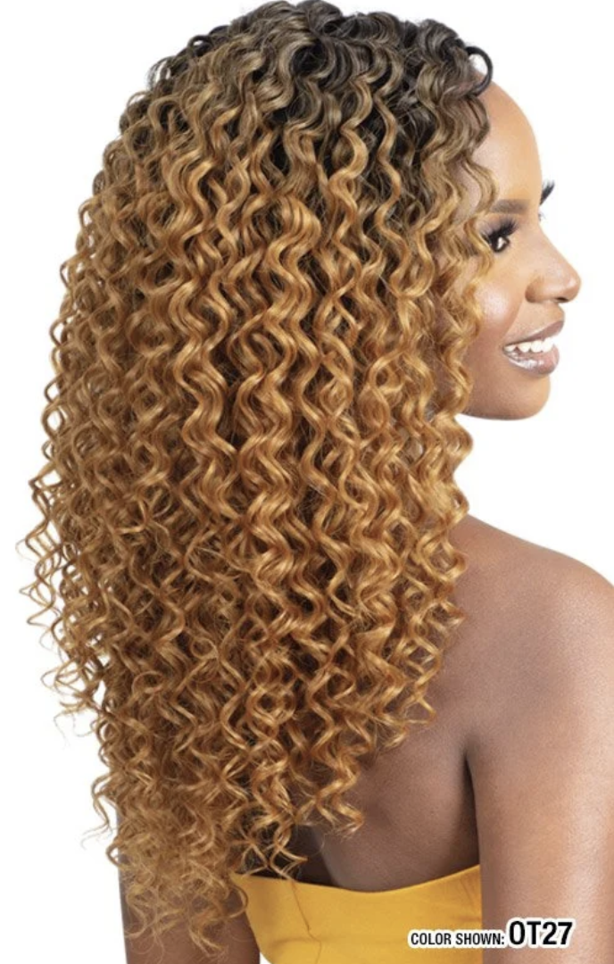 A woman shown in side profile wearing a long, curly wig with dark roots and warm honey-blonde highlights. The image is cropped to show the hair product, with part of the model's shoulder and strap visible.