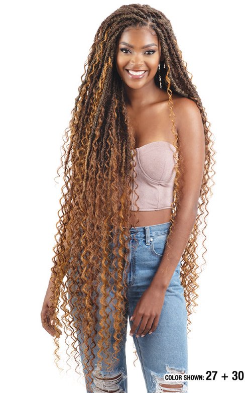 Woman with long, curly hair styled in braids, wearing a strapless top and jeans.