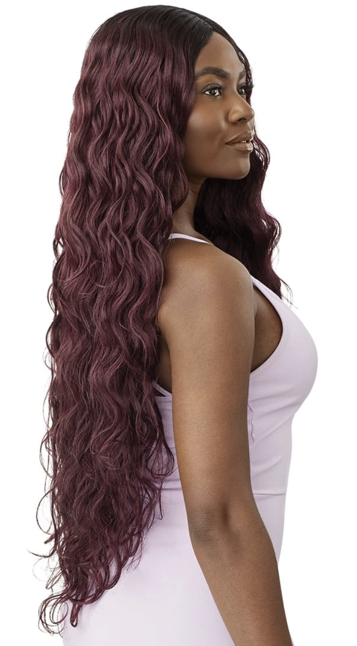 A woman shown from the back and side wearing a long, wavy wig in a deep burgundy-purple shade, paired with a light lavender tank top against a plain white background.