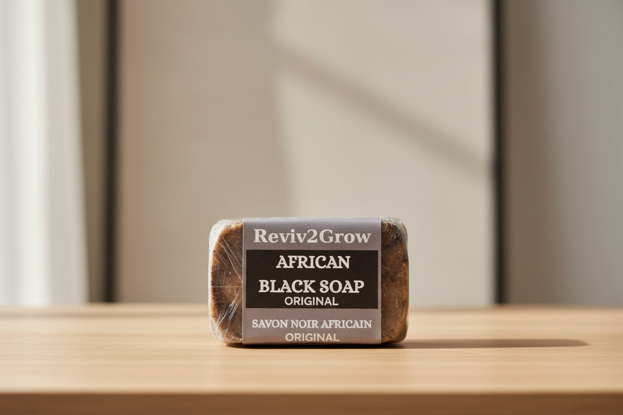 Bar of African Black Soap wrapped in clear plastic with 'Reviv2Grow' branding on a wooden surface.