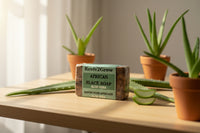 Thumbnail for Bar of African Black Soap with aloe vera on a table with potted aloe plants