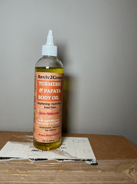 Thumbnail for Bottle of Reviv2Glow Turmeric & Papaya Body Oil on a cardboard surface with a gray background