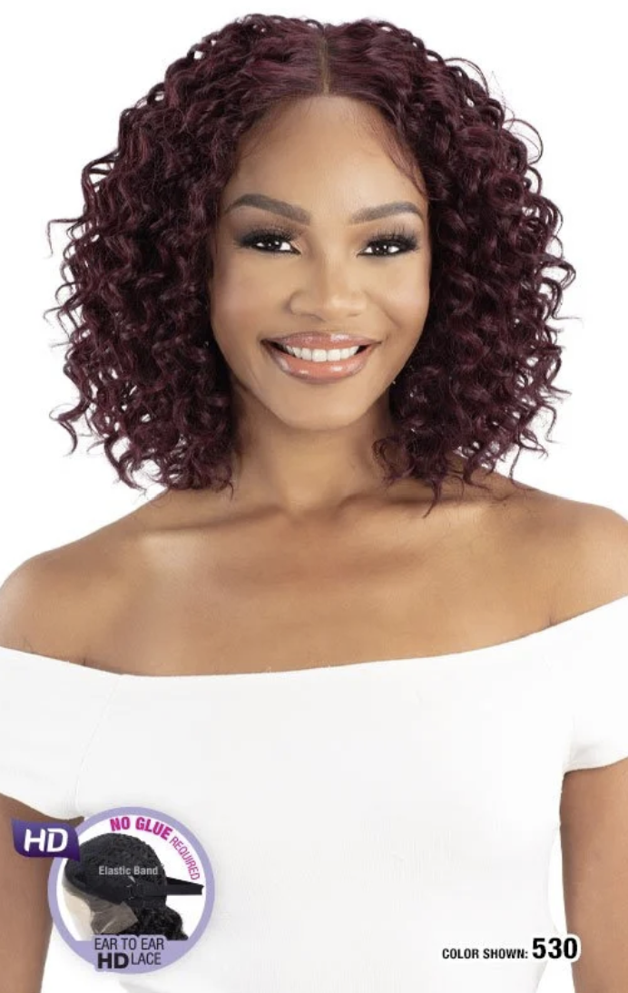 Woman with styled hair, wearing a white top, with a brand logo in the corner.